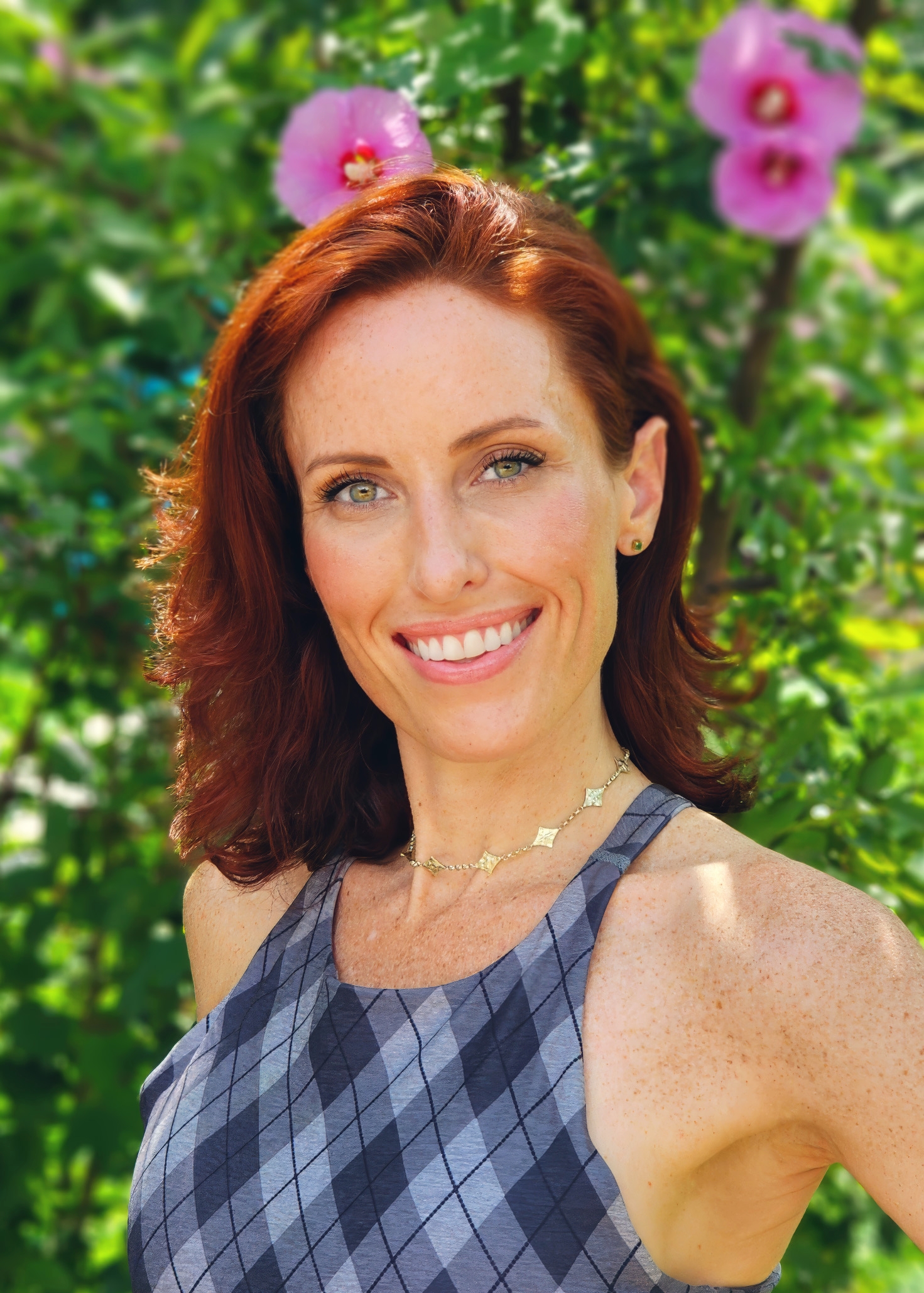 Mary-Kate Seward, founder of Beacon Ranch Studio, smiling in a blue patterned top against a background of green foliage and pink flowers